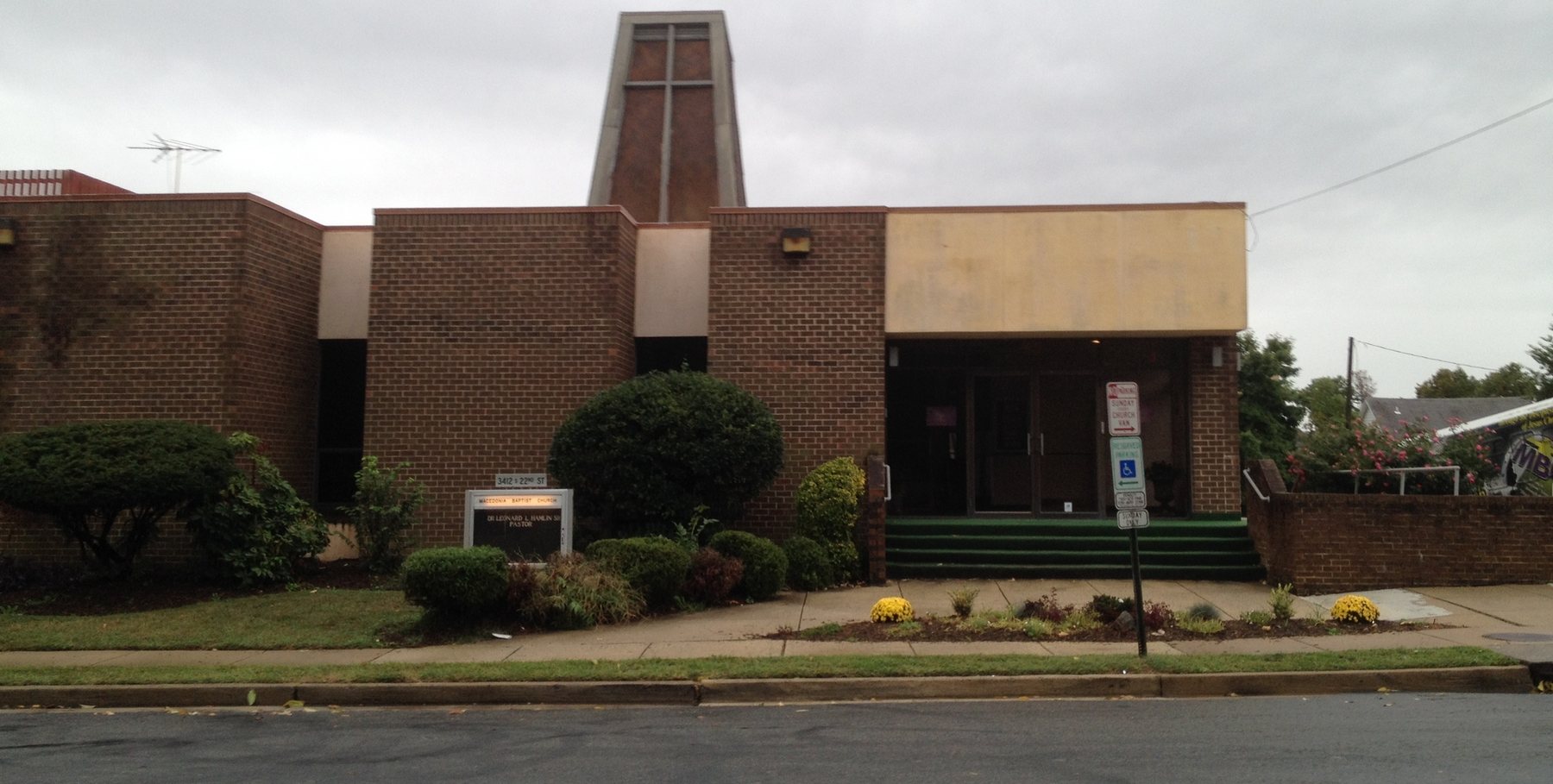 The Macedonia Baptist Church building and bell tower, in an earlier photograph. The sign out front names a former pastor.